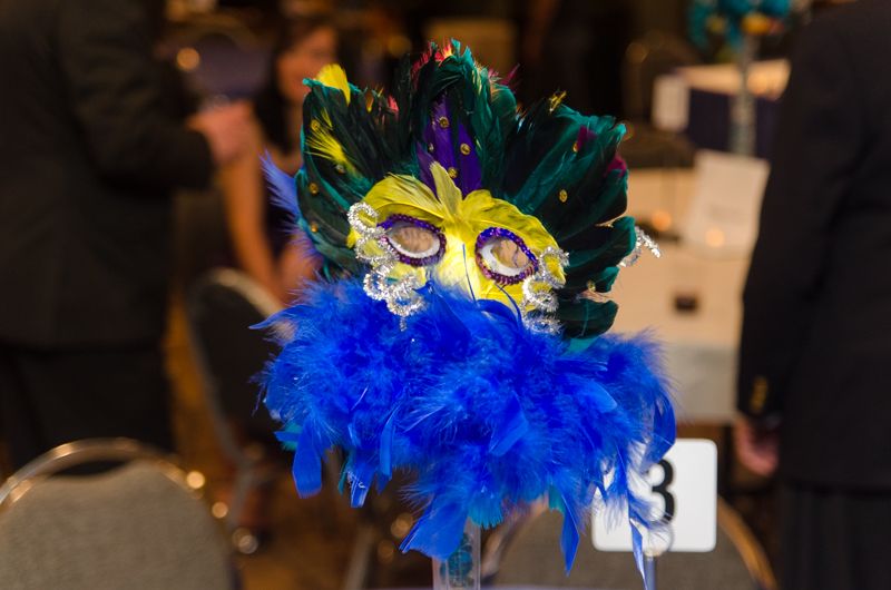 A blue and green feathered masquerade mask centrepiece on a banquet table