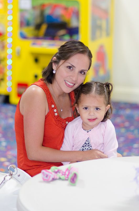 A smiling mother hugging her young daughter at a table in a play centre