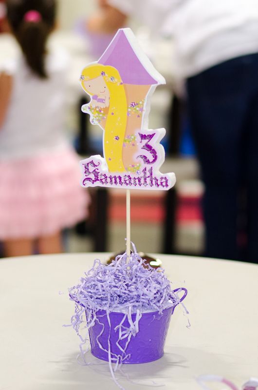 A Rapunzel-themed number 3 cake topper rising from a purple centrepiece bucket