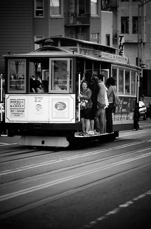Black-and-white photo of a Powell and Market cable car full of riders climbing a San Francisco street