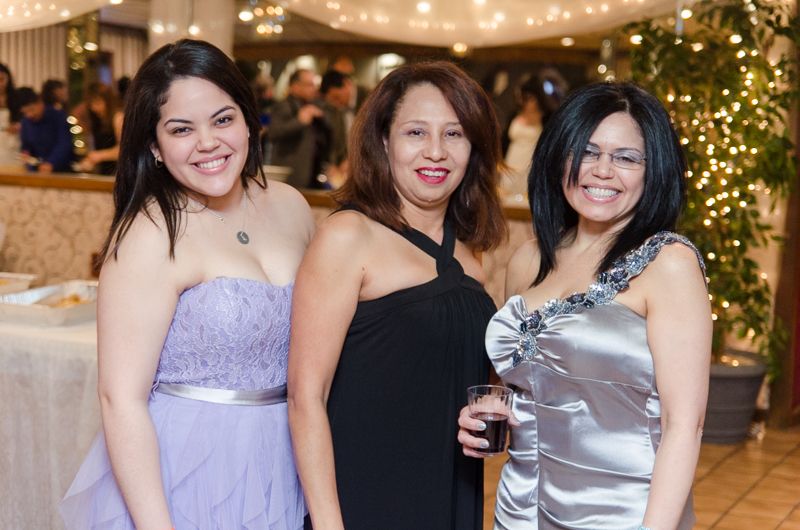 Three smiling women in evening gowns posing together at a party