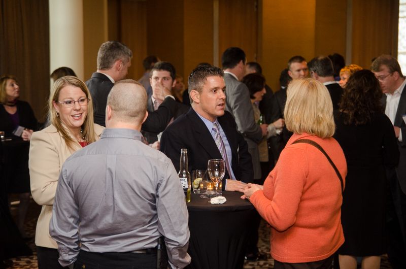 Guests in business attire chatting around cocktail tables at an evening reception