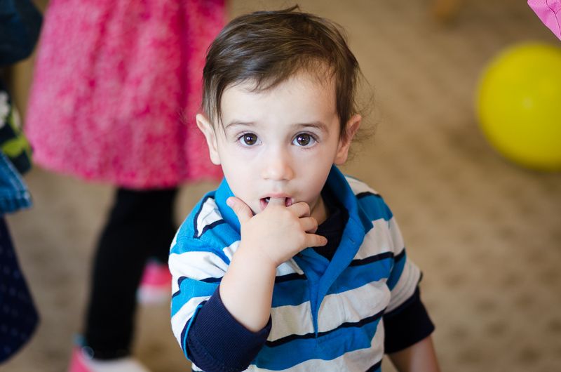 A toddler in a striped shirt with his fingers in his mouth, looking straight at the camera