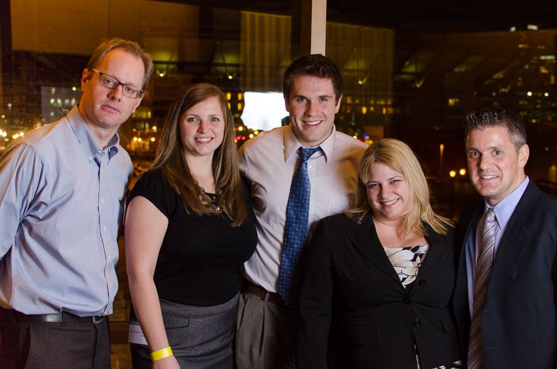 Five colleagues posing together in front of a window overlooking the city lights at night