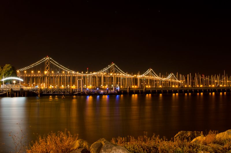 The San Francisco–Oakland Bay Bridge lit up at night, its lights reflected in the bay
