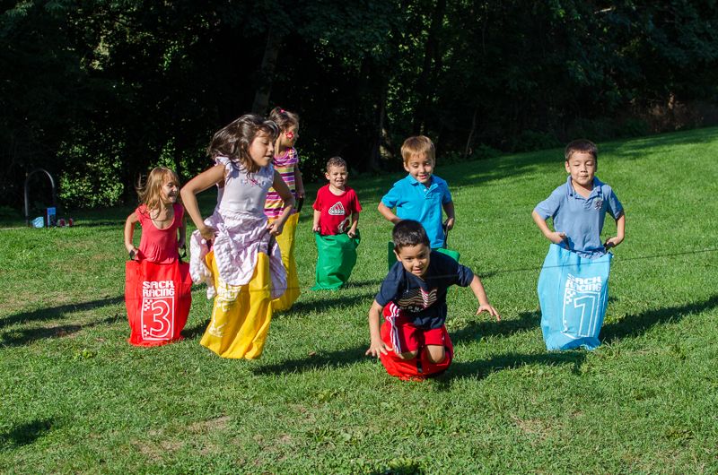 Children hopping across a grassy park in colourful sack-race bags