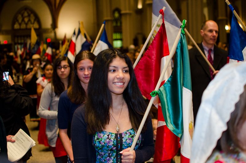 A smiling teenage girl carrying the Mexican flag in a procession of flags through a cathedral