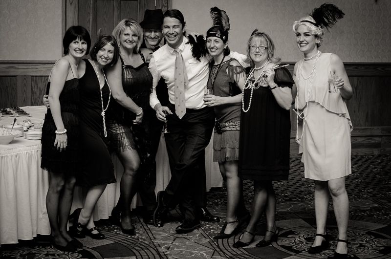 Black-and-white group photo of partygoers in 1920s flapper dresses, pearls and feathered headbands