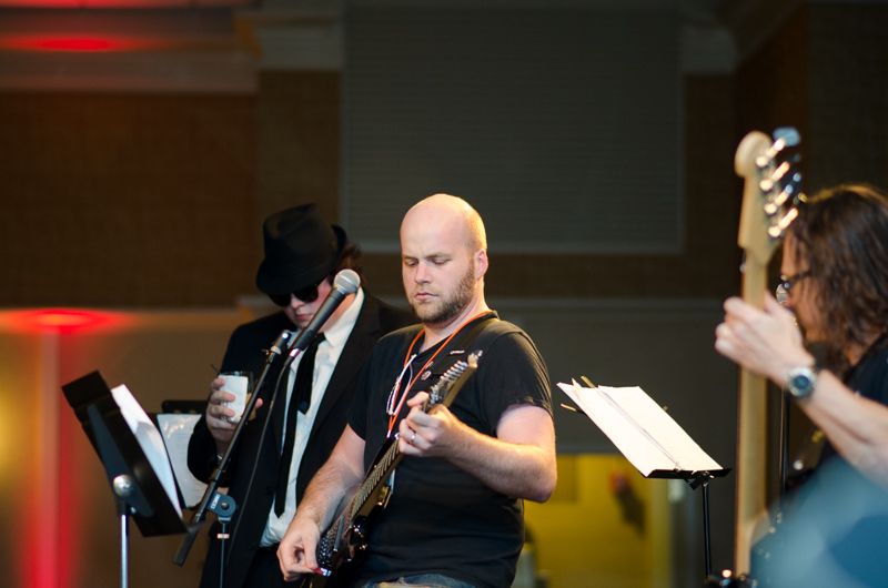 A bald guitarist concentrating as he plays in a band at an 80s-themed party