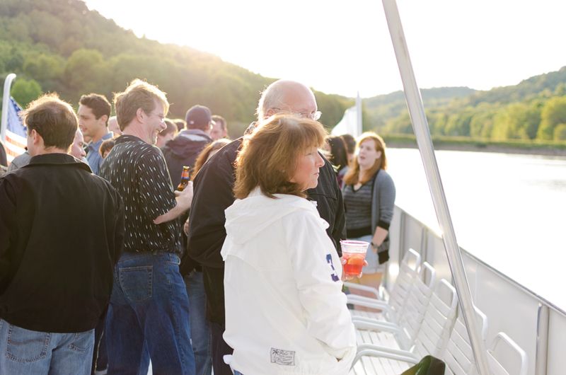 Guests at the rail of a riverboat cruising between green hills in late-afternoon sun