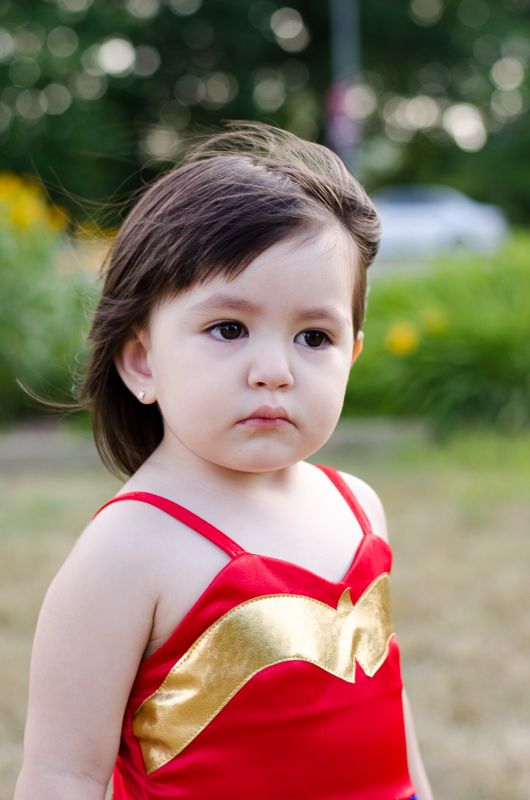 A serious little girl in a red and gold Wonder Woman top, outdoors among summer flowers