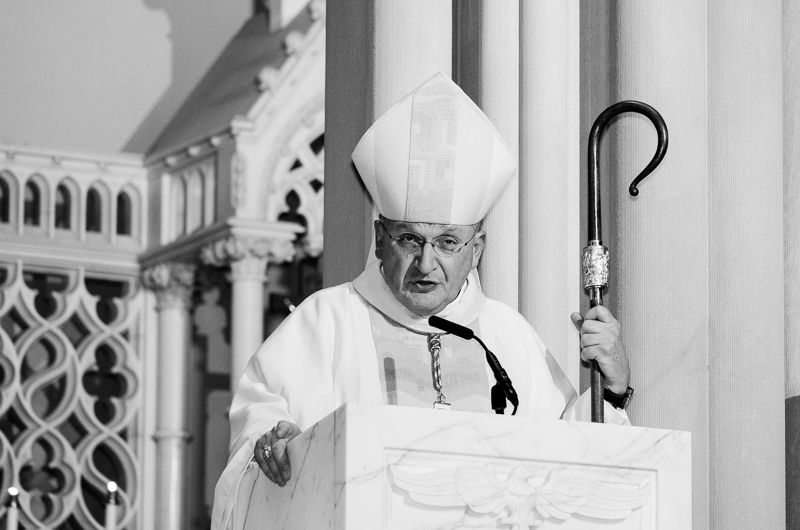 Black-and-white photo of a bishop in a mitre preaching from a pulpit, holding his crozier