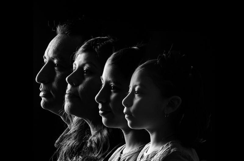 Black-and-white low-key portrait of four family members in profile, one behind the other