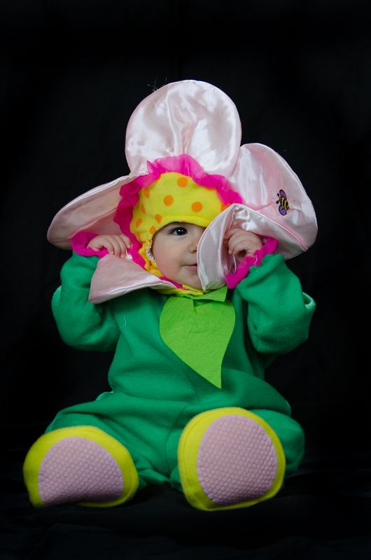 A baby in a green and pink flower costume against a black backdrop