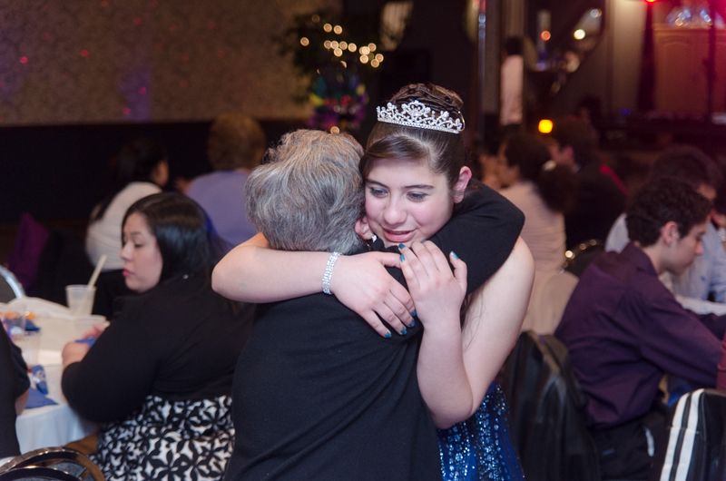 A girl in a tiara and sparkling blue gown hugging her grandmother at her party