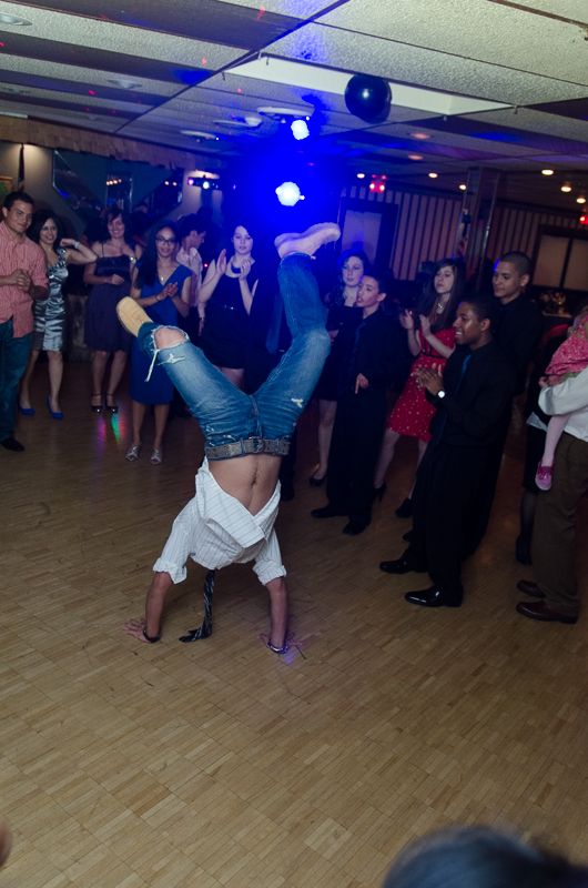 A young man doing a one-handed handstand on the dance floor as the crowd watches