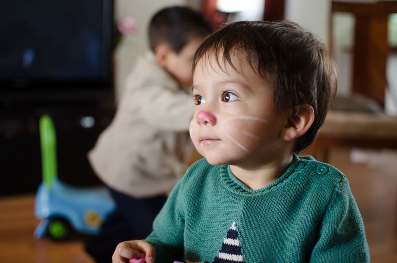 A toddler with a painted pink bunny nose and whiskers, gazing off to the side