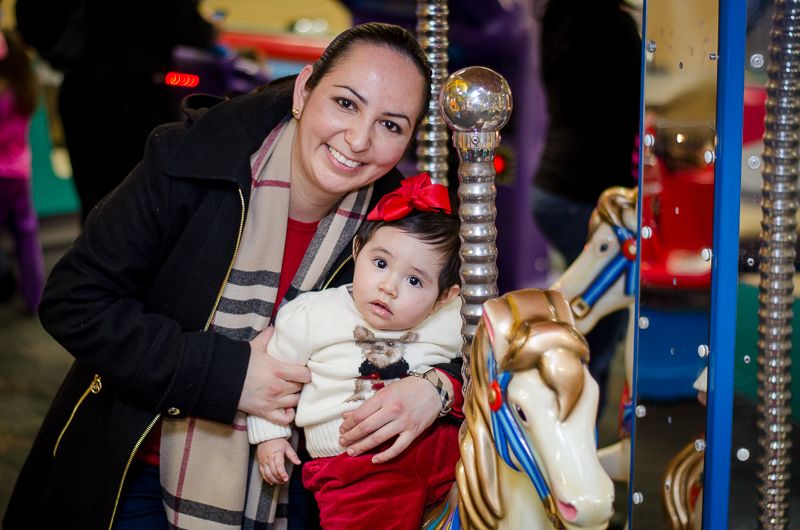 A smiling mother holding her baby daughter beside a white carousel horse