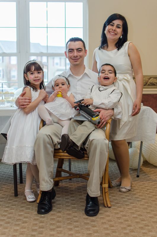 A family dressed in white for a baptism celebration, the father seated with the children on his lap