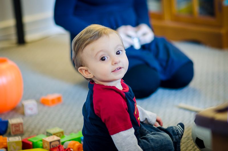 A toddler sitting among wooden blocks, glancing back over his shoulder at the camera