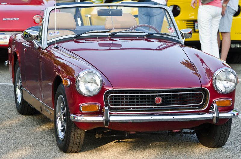 A glossy burgundy vintage MG convertible at a classic car show