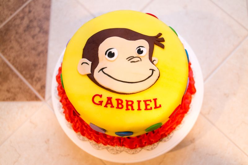 Top-down view of a yellow Curious George birthday cake with a child's name piped in red