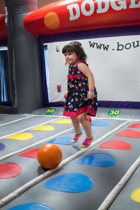 A little girl in a flowered dress jumping on a colourful inflatable bounce floor