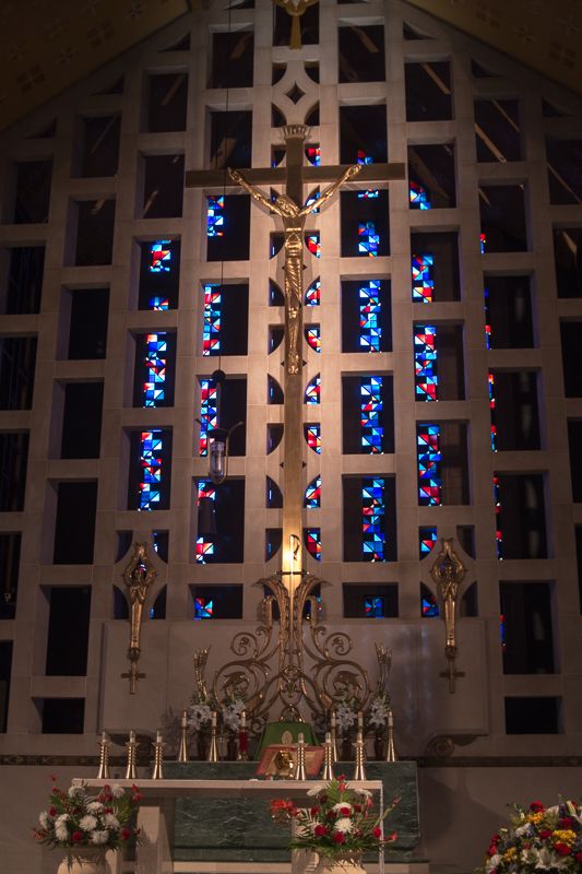 A church altar beneath a crucifix framed by a wall of blue and red stained glass