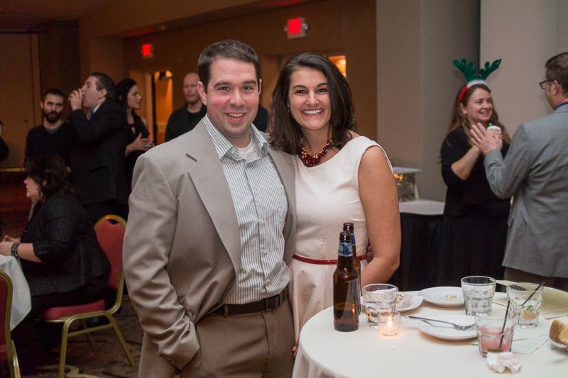 A couple posing beside a dinner table at a holiday party as guests mingle behind them