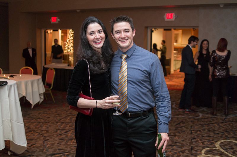 A smiling couple in evening wear posing at a holiday party in a hotel ballroom