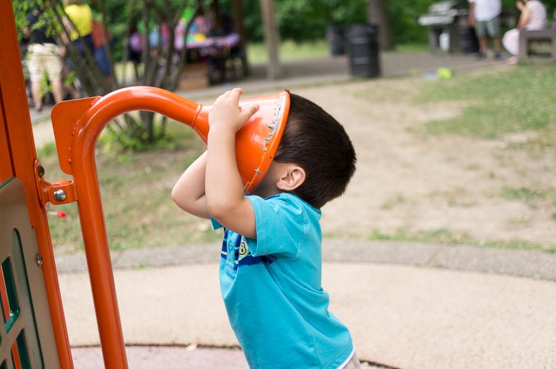 A boy holding a playground talk tube's orange horn over his face