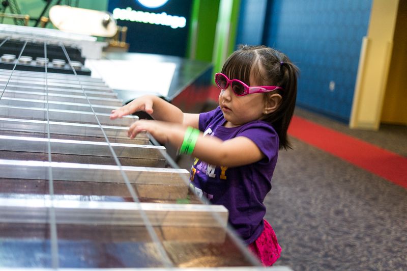A girl in pink sunglasses playing a giant xylophone exhibit at a children's museum