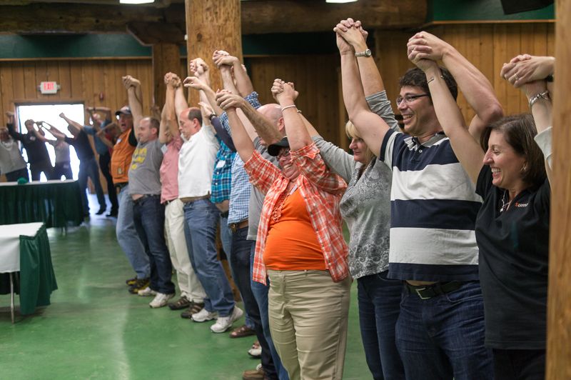 A line of colleagues holding hands raised overhead during a team-building exercise in a lodge hall